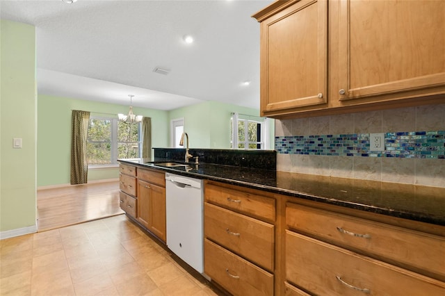 kitchen with tasteful backsplash, dark stone counters, white dishwasher, a chandelier, and a sink