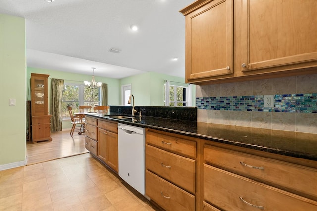 kitchen with tasteful backsplash, dark stone countertops, a sink, white dishwasher, and a notable chandelier