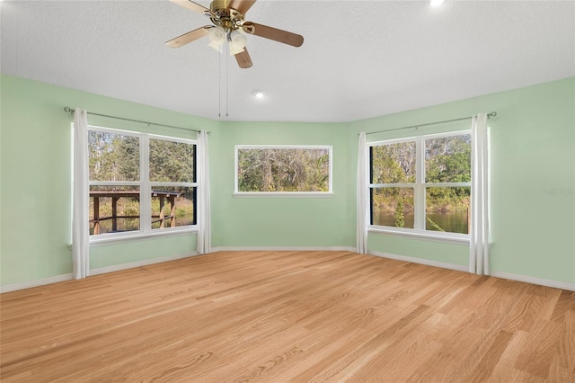 unfurnished room with light wood-type flooring, a ceiling fan, baseboards, and a textured ceiling