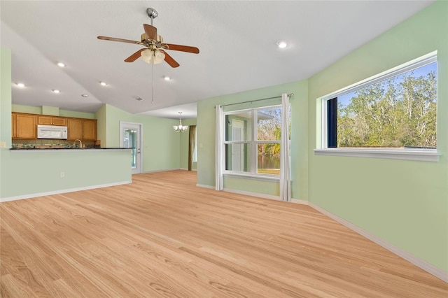 unfurnished living room with lofted ceiling, recessed lighting, ceiling fan with notable chandelier, baseboards, and light wood-style floors