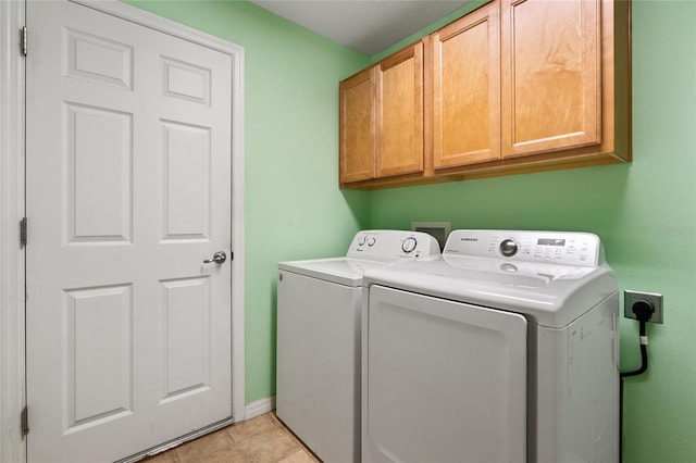 clothes washing area featuring light tile patterned floors, washing machine and clothes dryer, cabinet space, and baseboards