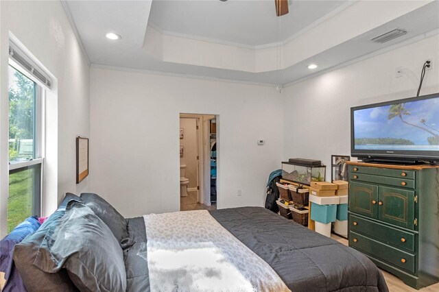 bedroom with a tray ceiling, ensuite bath, ceiling fan, and ornamental molding