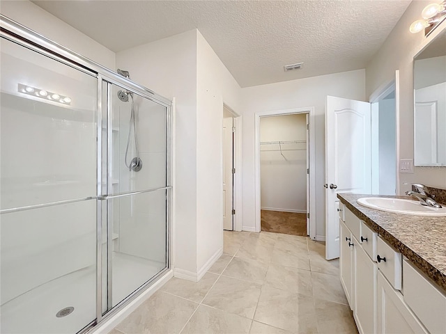 bathroom featuring tile patterned flooring, vanity, a shower with shower door, and a textured ceiling