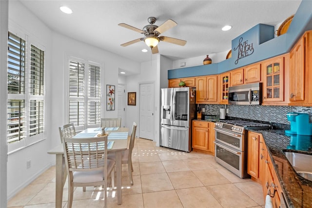 kitchen with dark stone counters, ceiling fan, light tile patterned floors, appliances with stainless steel finishes, and tasteful backsplash