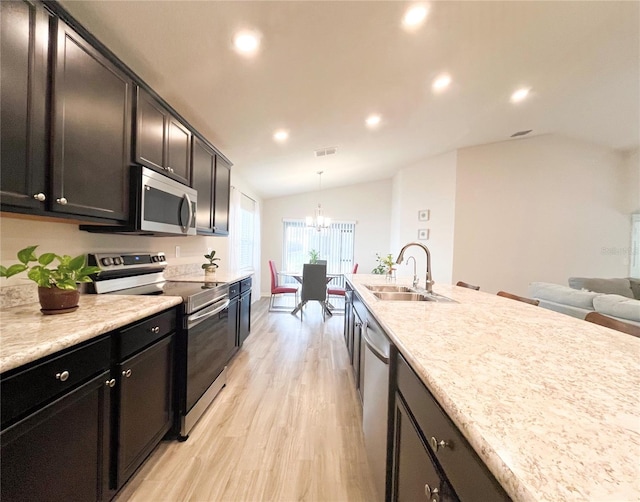 kitchen featuring sink, hanging light fixtures, vaulted ceiling, appliances with stainless steel finishes, and light wood-type flooring