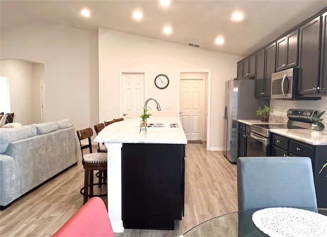 kitchen featuring a kitchen bar, a center island with sink, stainless steel appliances, and lofted ceiling