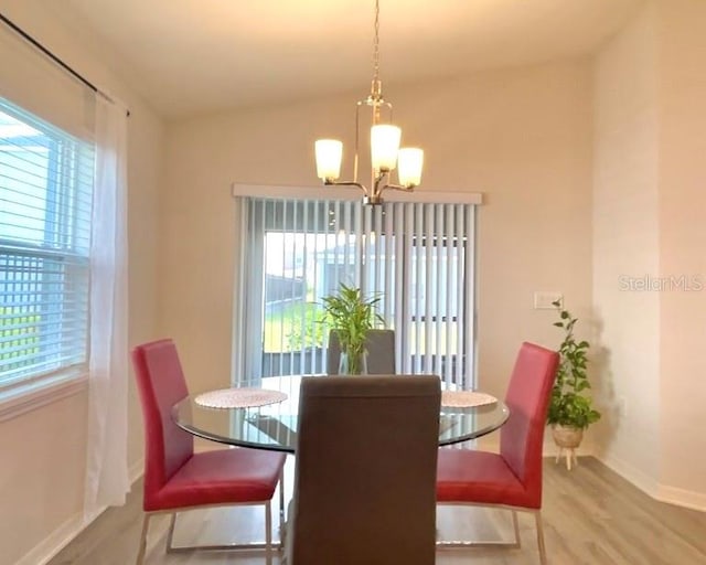 dining area featuring an inviting chandelier, a healthy amount of sunlight, lofted ceiling, and wood-type flooring