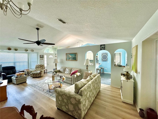 living room with a textured ceiling, lofted ceiling, light wood-type flooring, and ceiling fan with notable chandelier