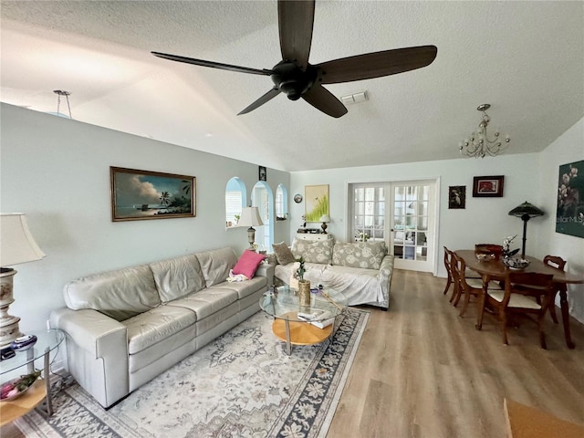 living room with ceiling fan with notable chandelier, vaulted ceiling, a textured ceiling, a wealth of natural light, and wood-type flooring