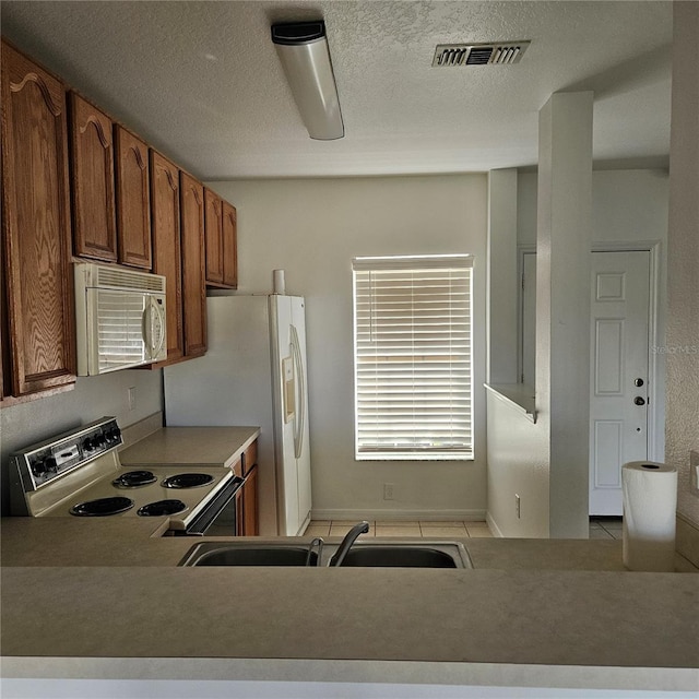 kitchen featuring sink, white appliances, a textured ceiling, and light tile patterned floors