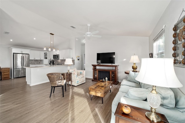 living room with light wood-type flooring, vaulted ceiling, ceiling fan, and sink