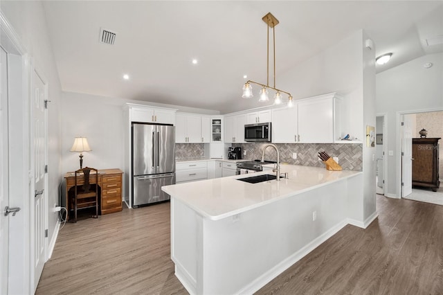 kitchen with lofted ceiling, sink, appliances with stainless steel finishes, decorative light fixtures, and white cabinetry