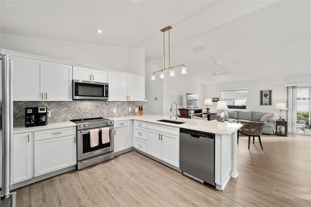 kitchen with stainless steel appliances, sink, white cabinets, hanging light fixtures, and lofted ceiling