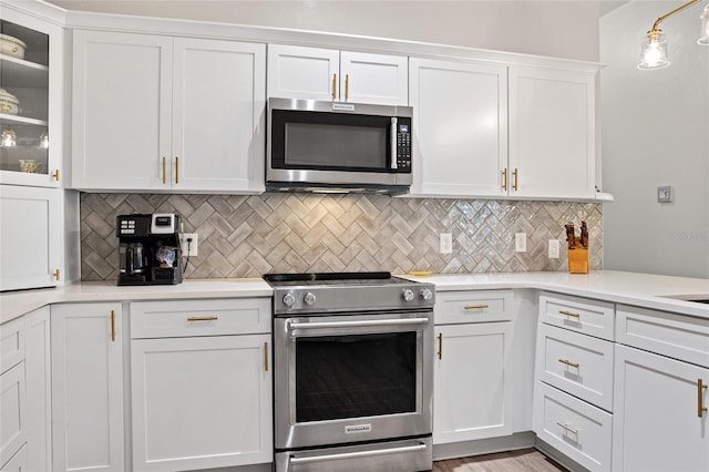 kitchen featuring pendant lighting, white cabinets, light hardwood / wood-style flooring, tasteful backsplash, and stainless steel appliances