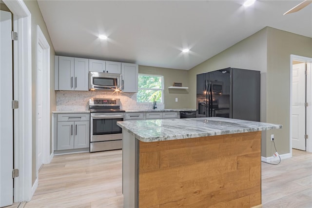 kitchen with light stone counters, a kitchen island, light hardwood / wood-style floors, and appliances with stainless steel finishes