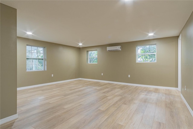 basement featuring light hardwood / wood-style floors, a healthy amount of sunlight, and an AC wall unit