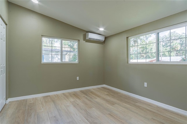 empty room featuring a wall mounted air conditioner, lofted ceiling, and light wood-type flooring