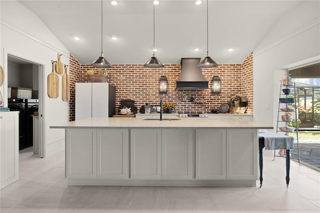 kitchen with a center island with sink, custom exhaust hood, pendant lighting, and brick wall