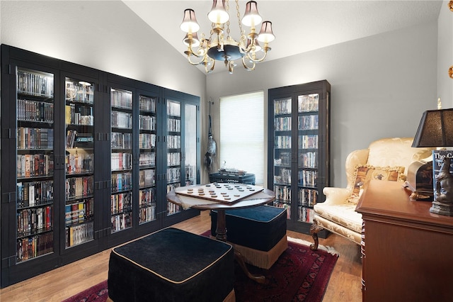 sitting room with lofted ceiling, a notable chandelier, wall of books, and wood finished floors