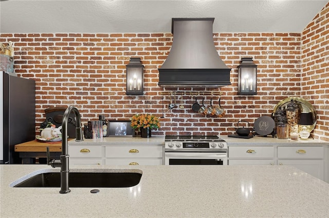 kitchen featuring appliances with stainless steel finishes, white cabinets, a sink, light stone countertops, and premium range hood