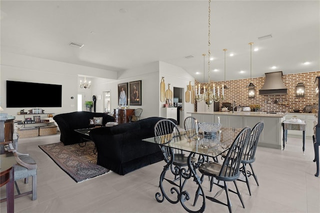 dining space with light tile patterned floors, brick wall, a chandelier, and vaulted ceiling