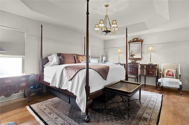 bedroom with a chandelier, a raised ceiling, wainscoting, and wood finished floors