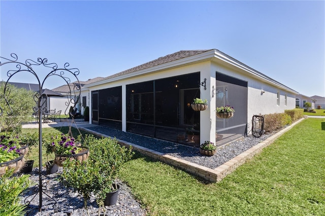 back of house featuring a yard, a sunroom, and stucco siding