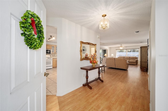 corridor with a chandelier, light hardwood / wood-style floors, and a textured ceiling