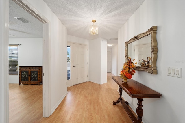 foyer entrance featuring a notable chandelier, a textured ceiling, and light hardwood / wood-style flooring