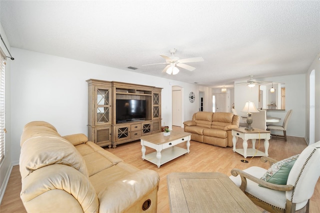 living room with a textured ceiling, light hardwood / wood-style flooring, and ceiling fan