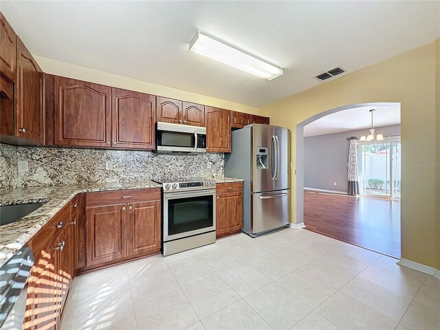 kitchen featuring light stone countertops, a notable chandelier, backsplash, light tile patterned floors, and appliances with stainless steel finishes