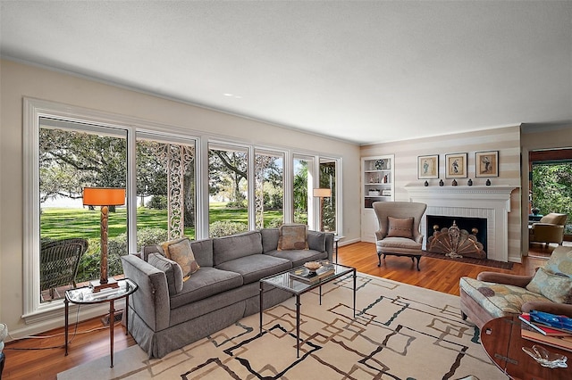 living room featuring built in shelves, light wood-type flooring, and a brick fireplace