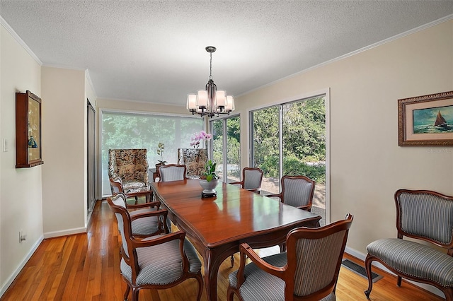 dining area with a textured ceiling, light wood-type flooring, ornamental molding, and a chandelier