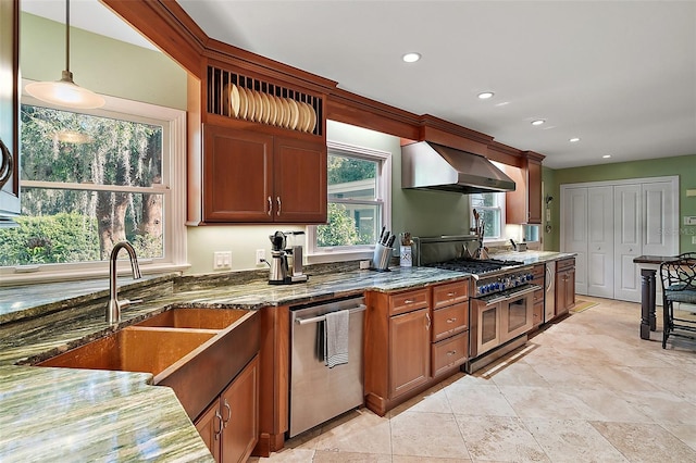 kitchen featuring sink, hanging light fixtures, stainless steel appliances, wall chimney range hood, and dark stone counters