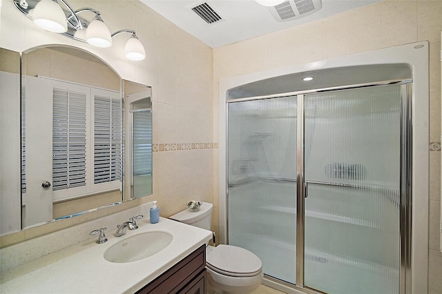 bathroom with a shower with door, vanity, tile walls, and toilet