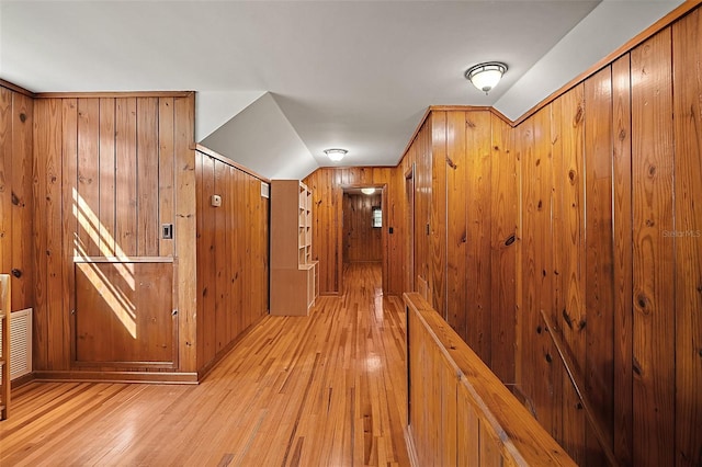 hall with wood walls, light hardwood / wood-style flooring, and vaulted ceiling