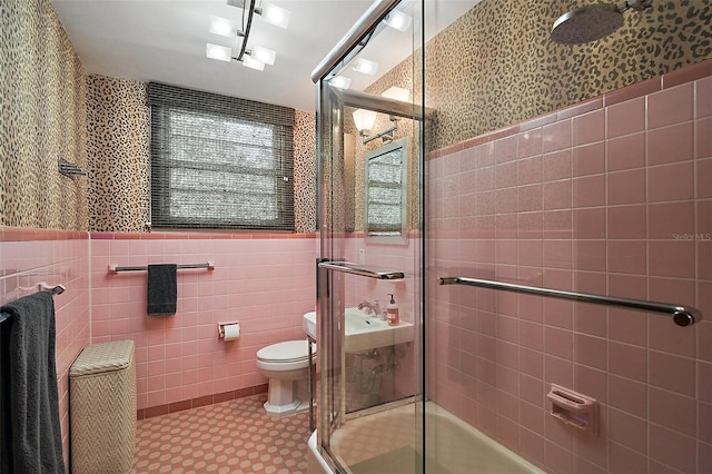 bathroom featuring toilet, a shower with shower door, and tile walls