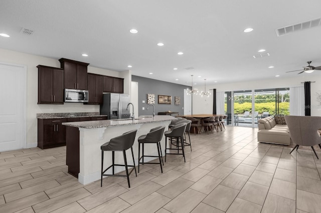 kitchen with a kitchen breakfast bar, light stone counters, ceiling fan with notable chandelier, stainless steel appliances, and a large island