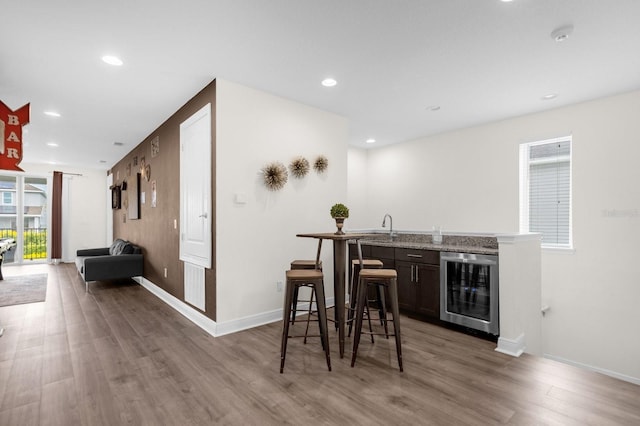 bar featuring wine cooler, hardwood / wood-style floors, dark brown cabinets, and sink