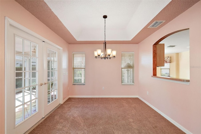 carpeted empty room with a raised ceiling, a textured ceiling, an inviting chandelier, and french doors