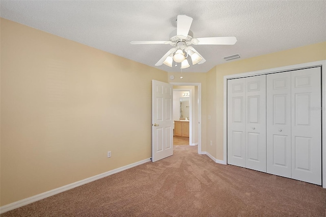 unfurnished bedroom featuring light carpet, a textured ceiling, a closet, and ceiling fan