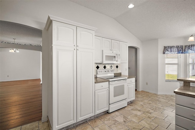 kitchen with lofted ceiling, white appliances, white cabinets, light wood-type flooring, and decorative light fixtures