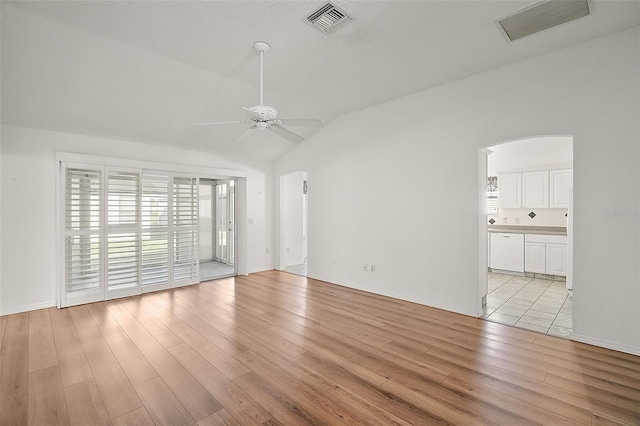 empty room with a textured ceiling, light wood-type flooring, vaulted ceiling, and ceiling fan