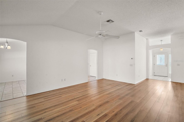 unfurnished living room with ceiling fan with notable chandelier, lofted ceiling, a textured ceiling, and light hardwood / wood-style flooring