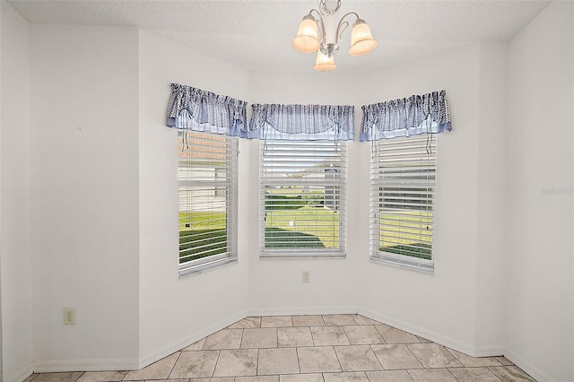 tiled spare room featuring a textured ceiling and an inviting chandelier