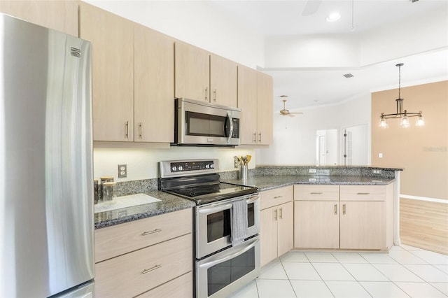 kitchen featuring appliances with stainless steel finishes, dark stone countertops, light brown cabinetry, and kitchen peninsula