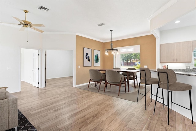 dining room with crown molding, ceiling fan with notable chandelier, and light wood-type flooring