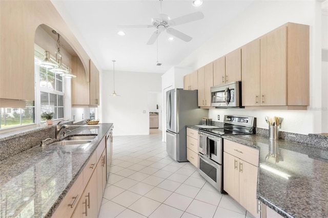 kitchen featuring light brown cabinets, appliances with stainless steel finishes, hanging light fixtures, and dark stone countertops