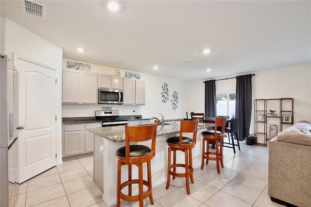 kitchen featuring a kitchen breakfast bar, stainless steel appliances, light tile patterned floors, white cabinetry, and an island with sink