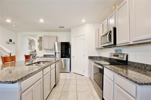 kitchen featuring sink, light tile patterned floors, an island with sink, appliances with stainless steel finishes, and stone countertops